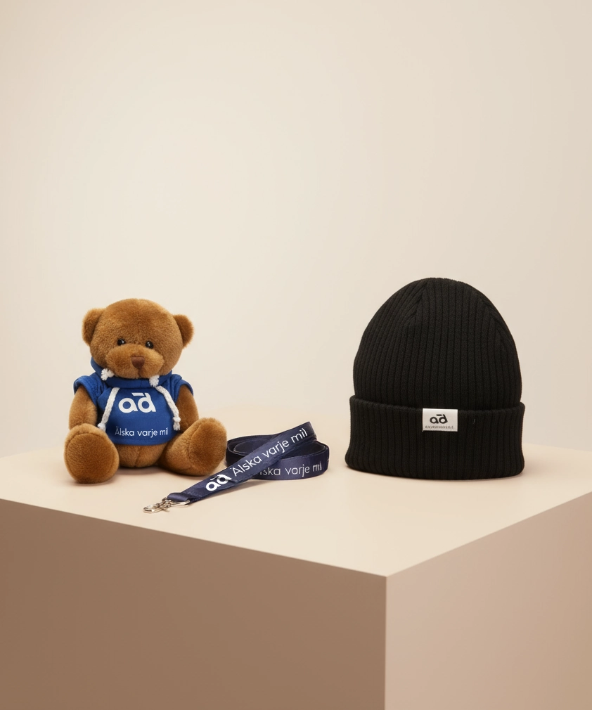AD Bildelar merchandise, inklusive en brun nallebjörn i en blå hoodie, en svart stickad mössa och en blå nyckelband där det står "Älska varje mil."